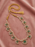 An ornate gold necklace with green and white stone accents, laid out on a dusty pink satin fabric background.