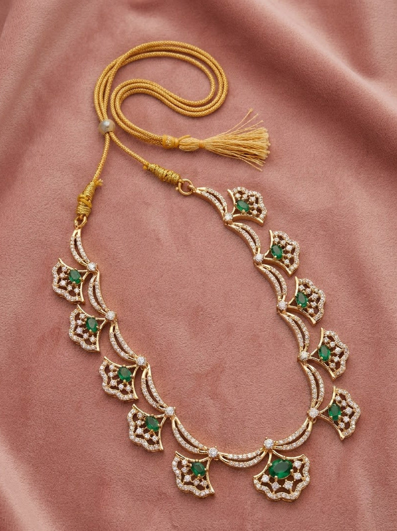 An ornate gold necklace with green and white stone accents, laid out on a dusty pink satin fabric background.