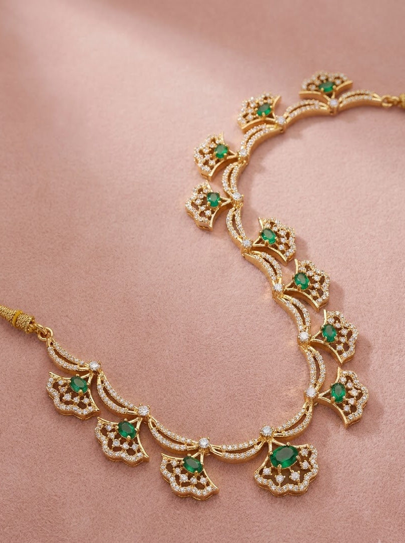 Gold-toned traditional necklace with green stone accents and small clear stones, arranged on a soft pink satin background.