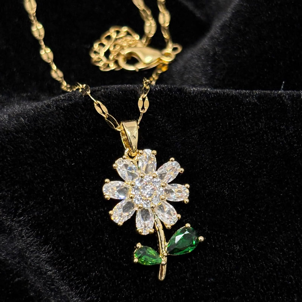 A gold flower pendant necklace with clear rhinestones and green marquise-cut stones, displayed on a black velvet background.