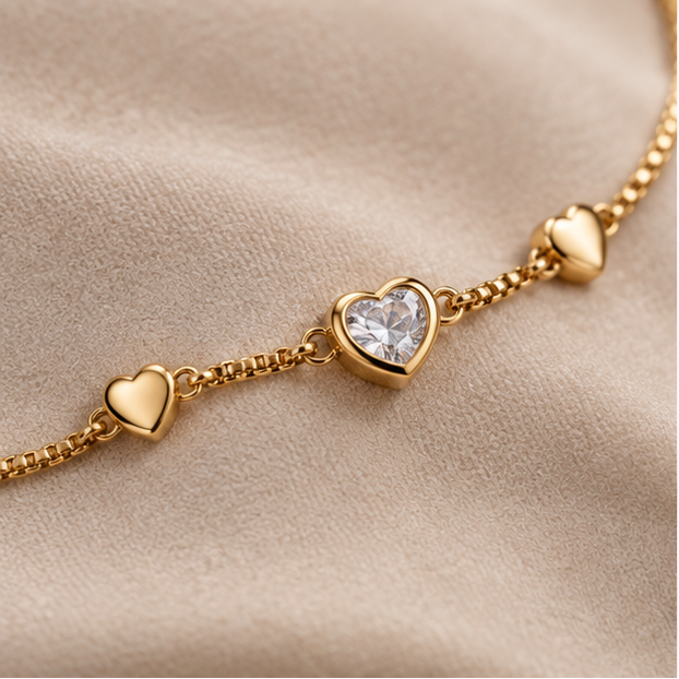 A collage showing a gold heart charm bracelet worn on a wrist and displayed flat. The bracelet features a delicate gold chain with multiple small gold hearts, including one larger heart with a clear heart-shaped crystal centerpiece.