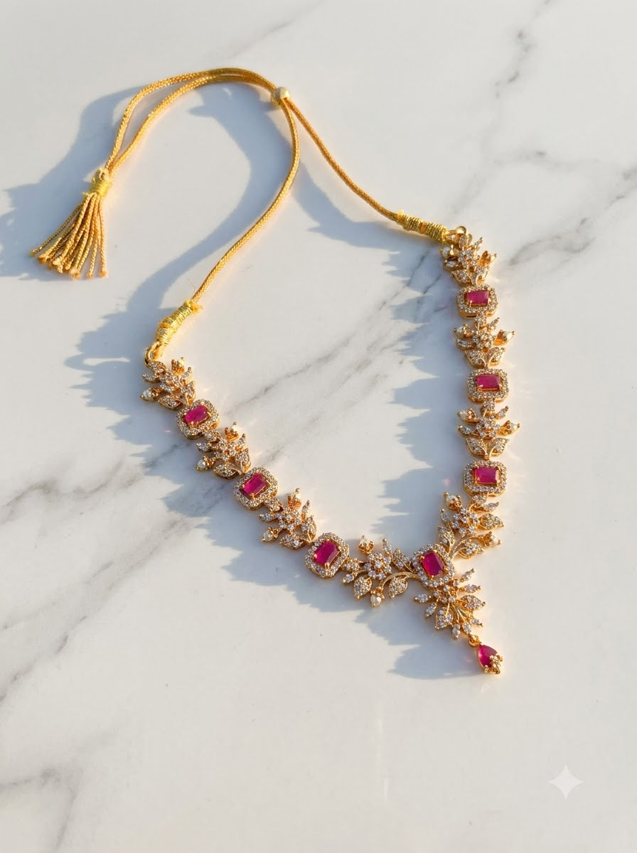 Ruby-toned jewelry necklace with multiple rectangular pink gemstones and a tassel, displayed on a white marble surface.
