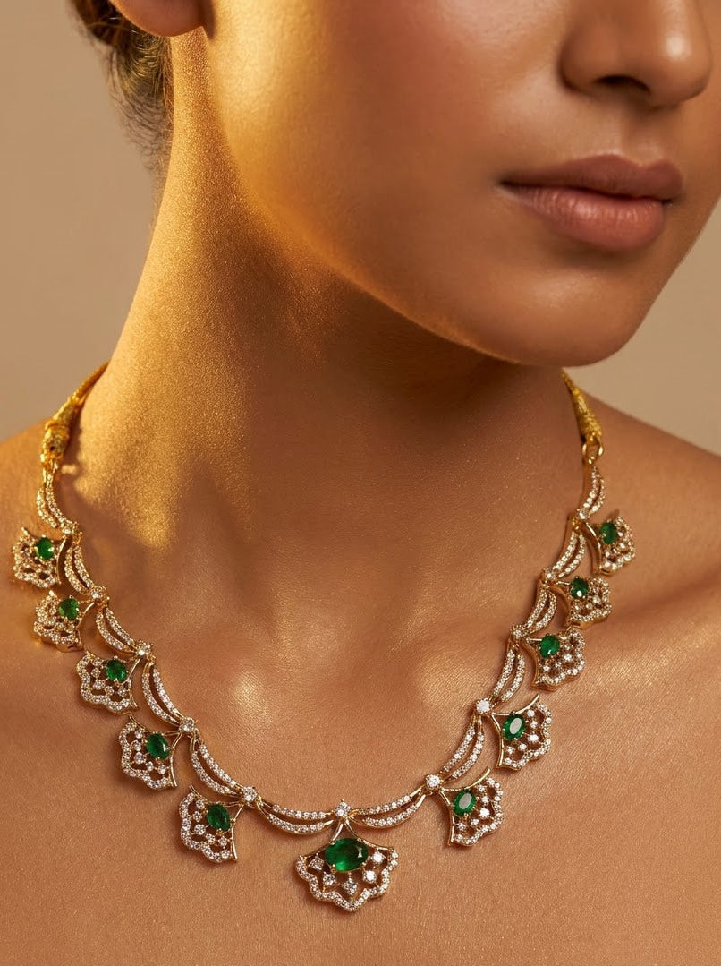 A close-up of a woman wearing an ornate gold necklace with green and white gemstone floral motifs against a warm beige background.